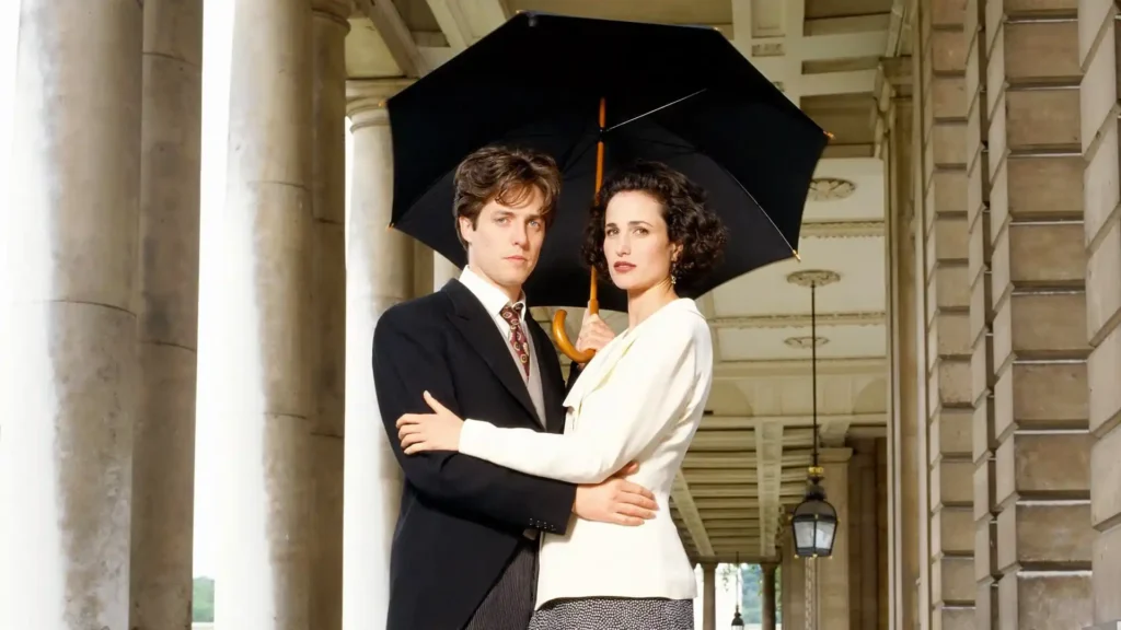 Hugh Grant e Andie MacDowell abraçados sob um guarda-chuva em cena de Quatro Casamentos e um Funeral.