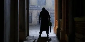 Cena do filme “O Massacre da Serra Elétrica: O Retorno de Leatherface” – Um personagem sombrio, segurando uma serra elétrica, aparece como uma silhueta em um corredor escuro e chuvoso.