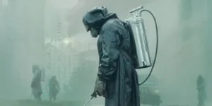 Cena da minissérie Chernobyl, mostrando um trabalhador em um traje de proteção contra radiação, segurando uma mangueira.
