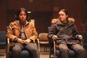 Dina (Isabella Merced) e Elle (Bella Ramsey) sentadas em cadeiras, são interrogadas pelo Conselho de Jackson em The Last of Us