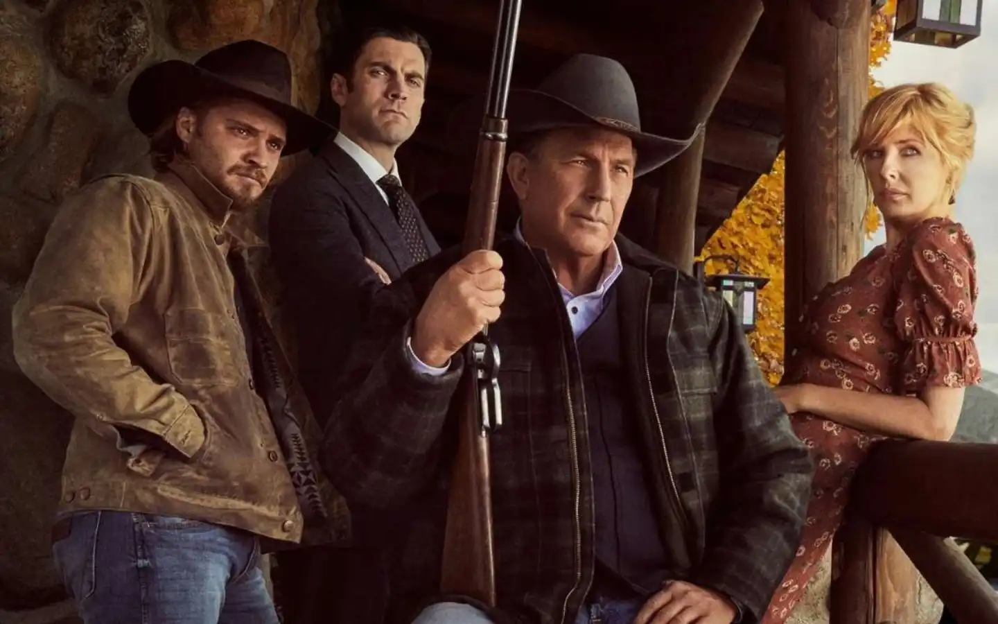 Personagens da série 'Yellowstone' posam em frente à varanda de uma cabana rústica. Um deles segura uma espingarda, reforçando o clima de tensão e poder da série.
