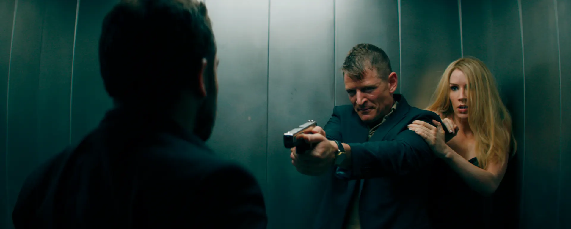 Philip Winchester aponta uma arma enquanto Charlotte Kirk observa em cena tensa de elevador em A Duquesa Vingadora
