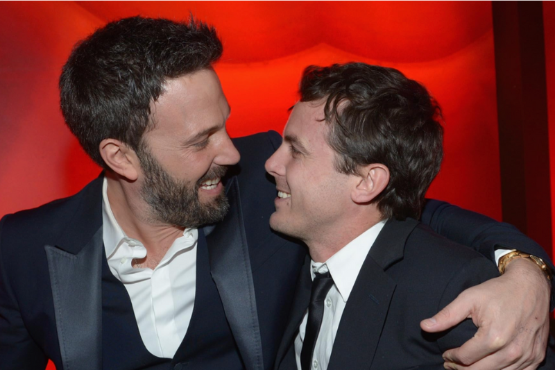 Ben Affleck e Casey Affleck sorrindo e abraçados em evento.