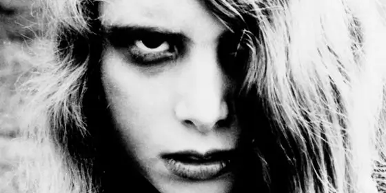 Imagen en blanco y negro de una joven con cabello largo y claro, parcialmente desordenado, en primer plano; escena característica de la película de terror La noche de los muertos vivientes.