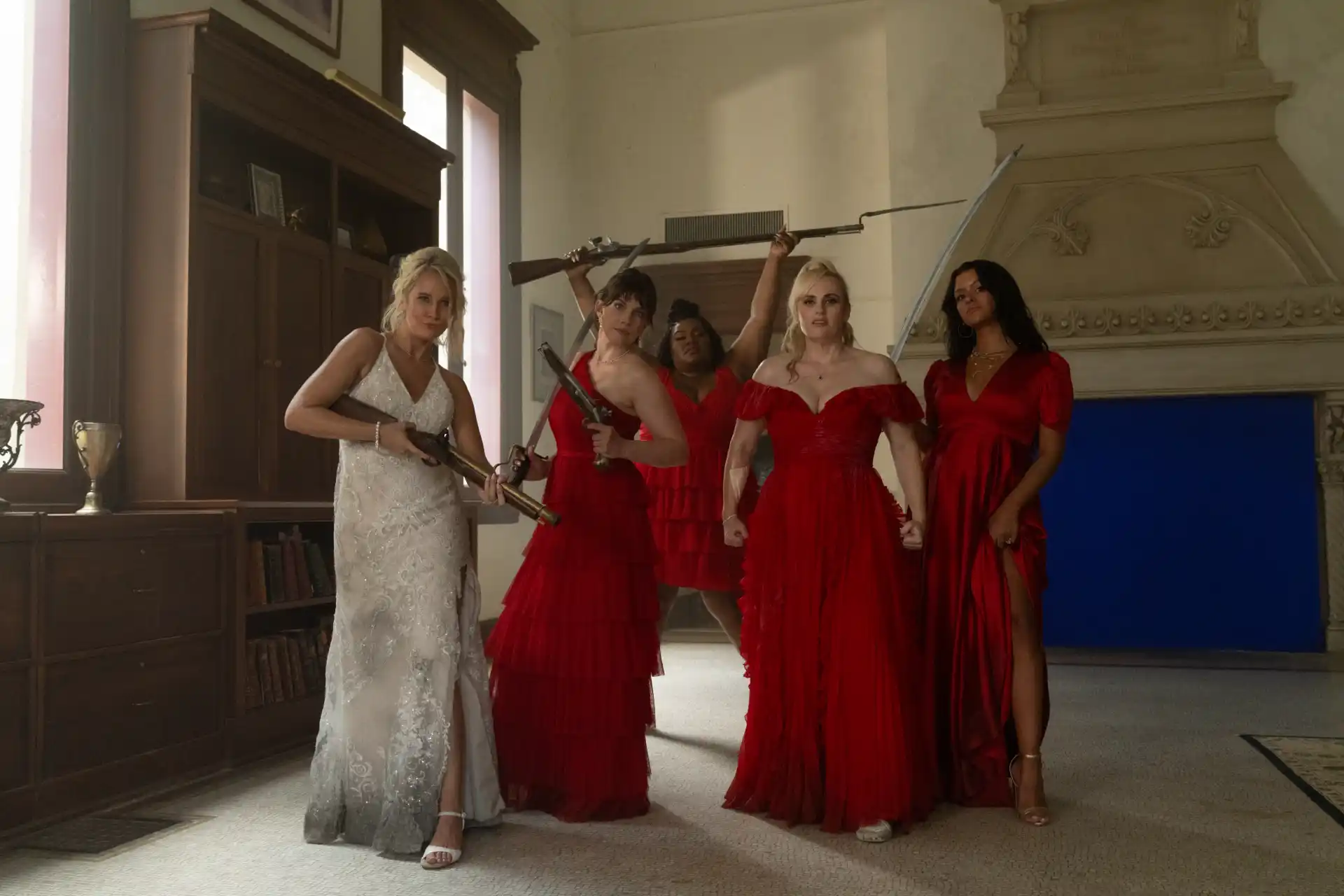 Rebel Wilson, Anna Camp e o elenco feminino vestem roupas de festa e seguram armas no filme Duro de Casar