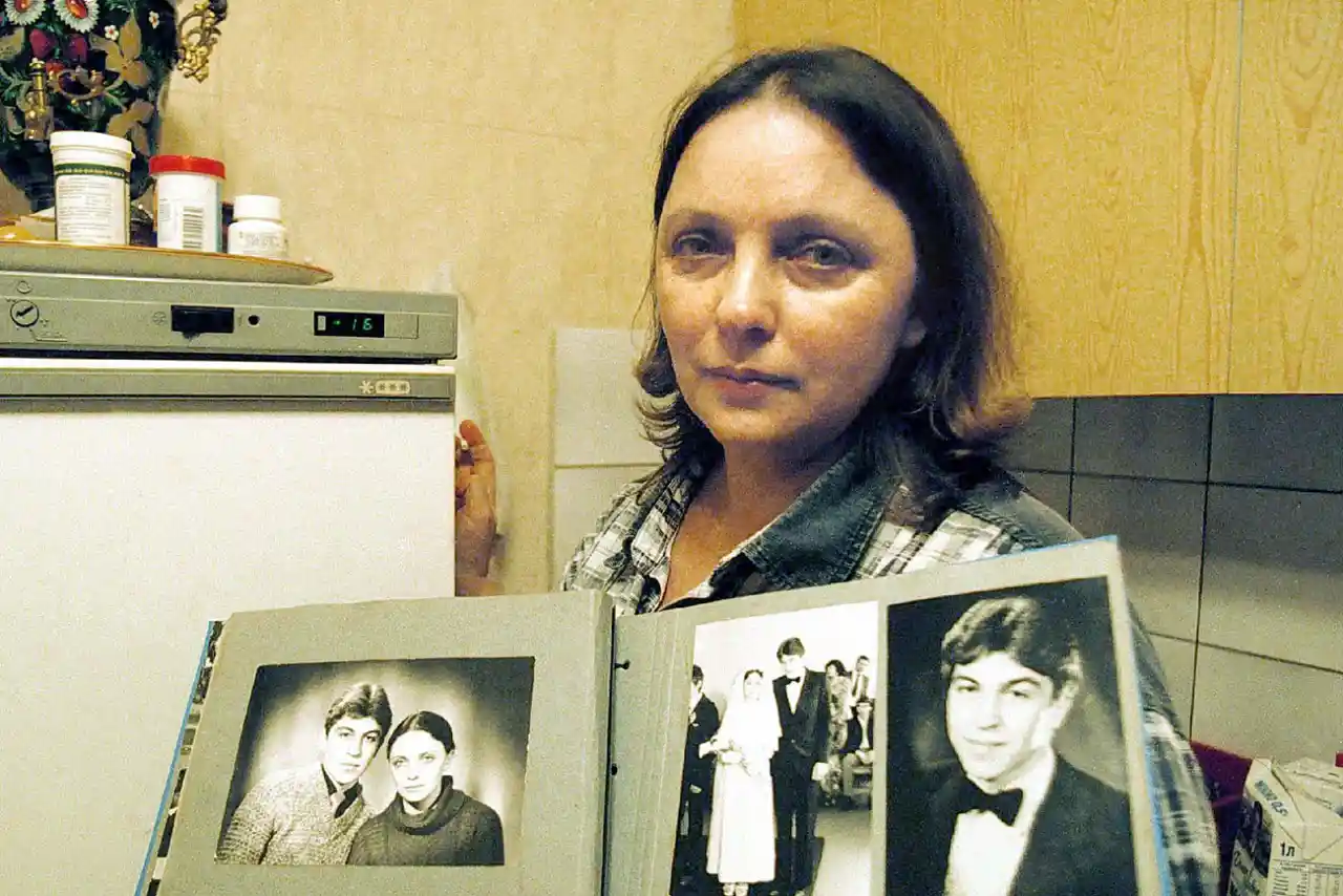 Foto da verdadeira Larisa Savitskaya segurando um álbum com fotos antigas dela e de seu falecido marido, Vladimir. Ela é a única sobrevivente do acidente aéreo de 1981