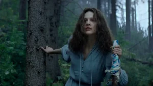 A atriz Nadezhda Kaleganova, interpretando Larisa Savitskaya, se apoia em uma árvore enquanto caminha pela floresta no filme A Única Sobrevivente