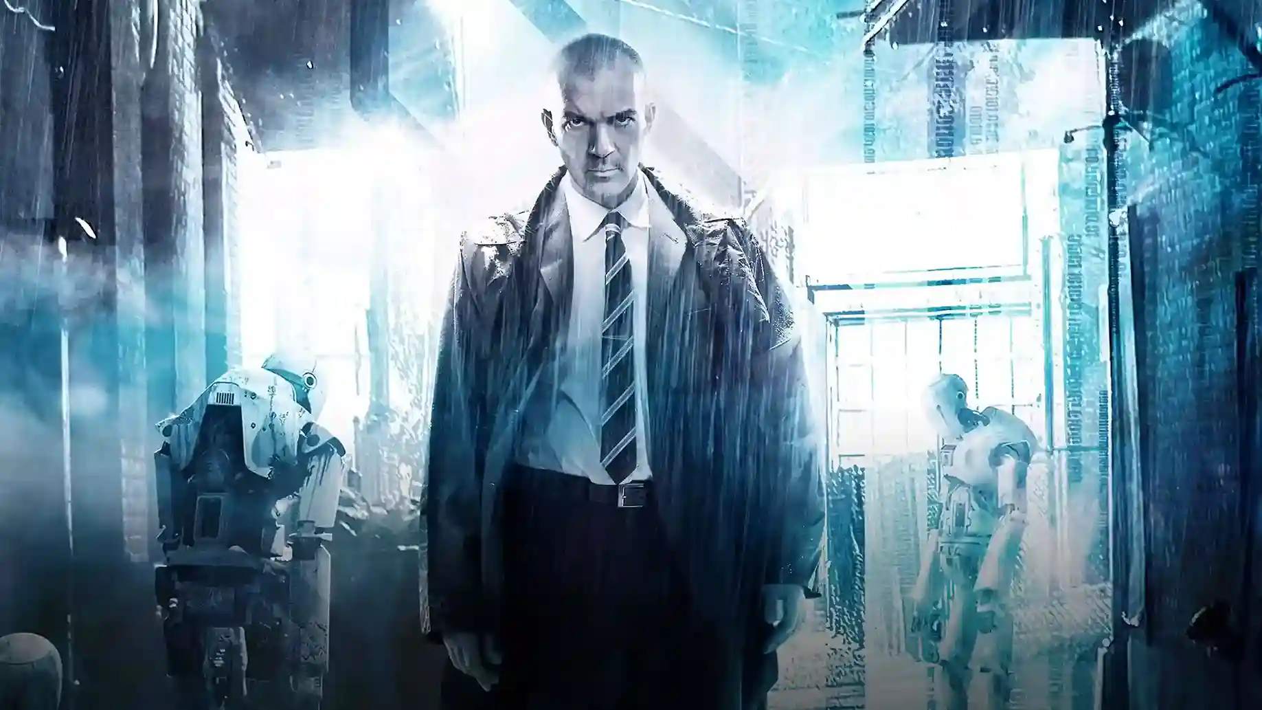 Imagen promocional de la película 'Autómata' (2014): hombre calvo con traje y corbata oscuros bajo la lluvia, de pie en un ambiente futurista y tecnológico con tonos azules, flanqueado por dos robots humanoides deteriorados en un pasillo industrial.(Crédito: The Movie Database - TMDB)