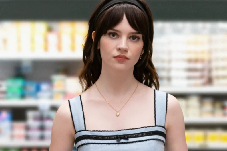 Sophie Thatcher looks serious, wearing a light dress, in a supermarket setting.