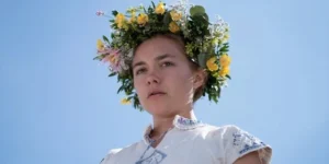 Florence Pugh em Midsommar com coroa de flores sob o céu azul.