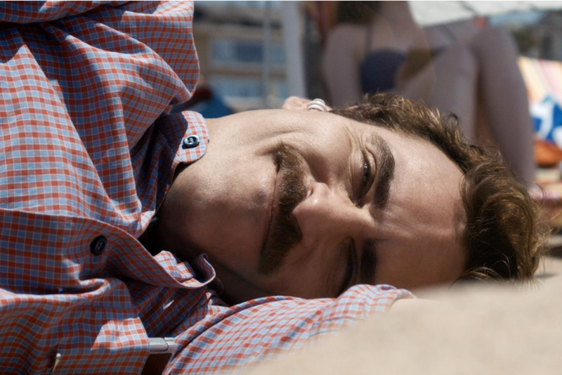 Joaquin Phoenix em cena de Ela, deitado na praia com fone no ouvido.