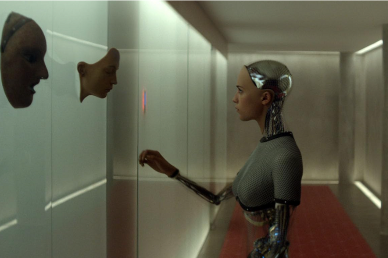 Ava, androide de Ex Machina, observa máscaras em uma parede de vidro.