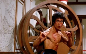 Escena de acción de la película Operación Dragón (1973) con Bruce Lee en posición de combate, mostrando su característica intensidad y destreza en artes marciales, probablemente enfrentando a uno de los secuaces de Han en la isla donde se desarrolla el torneo secreto de kung fu. (Credits: TMDB)