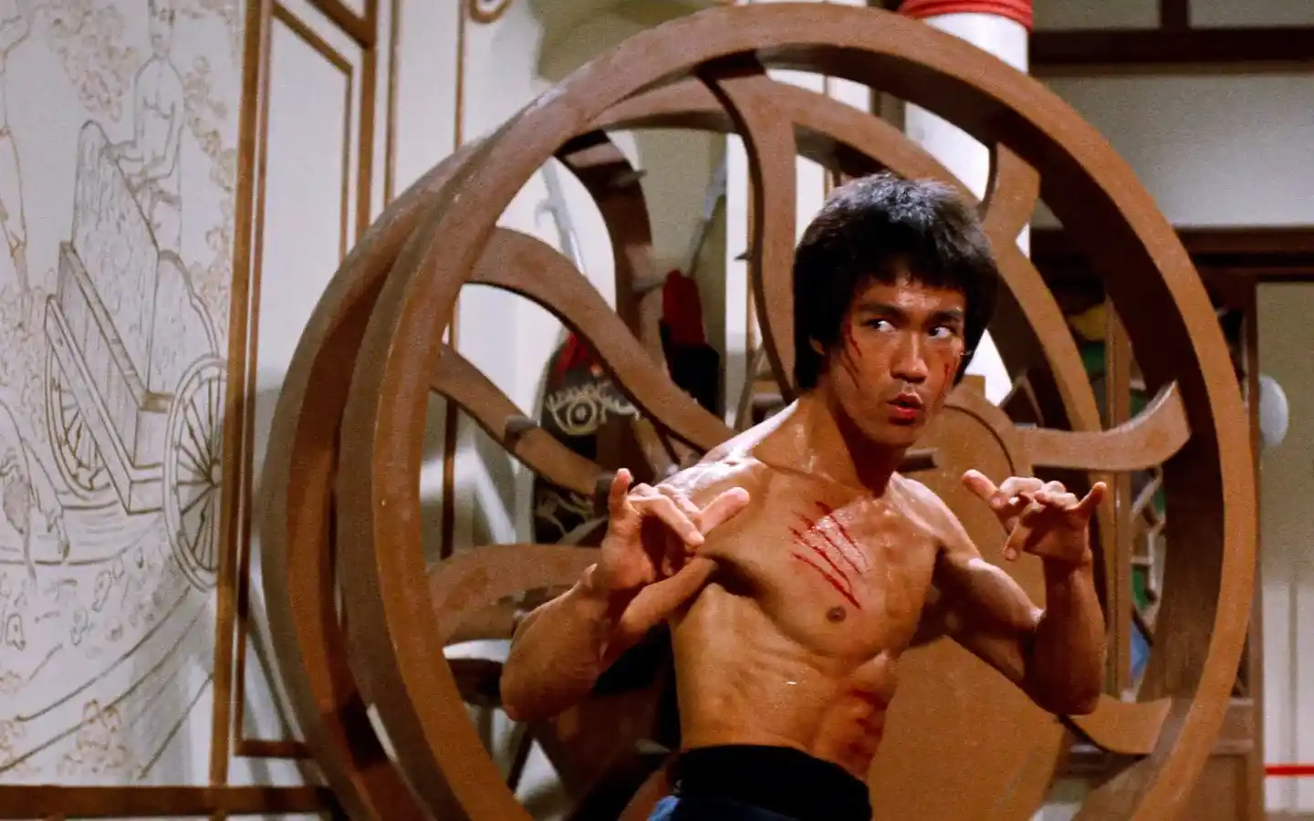 Escena de acción de la película Operación Dragón (1973) con Bruce Lee en posición de combate, mostrando su característica intensidad y destreza en artes marciales, probablemente enfrentando a uno de los secuaces de Han en la isla donde se desarrolla el torneo secreto de kung fu.
(Credits: TMDB)