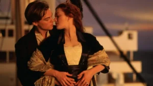 Romantic scene of couple embracing on ship's deck at sunset, man in dark coat holding woman in period dress.