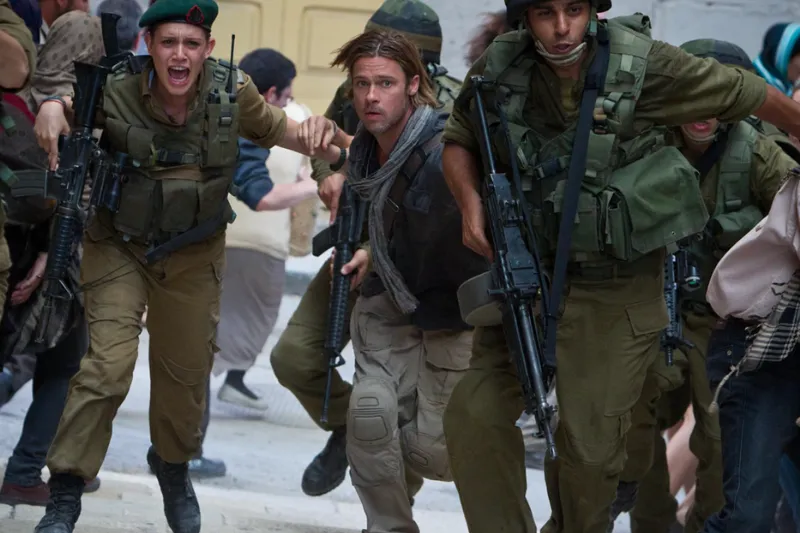 A man with long hair, surrounded by armed soldiers in military uniforms, moves urgently through a chaotic crowd; the atmosphere is tense, hinting at a crisis or dangerous situation.
