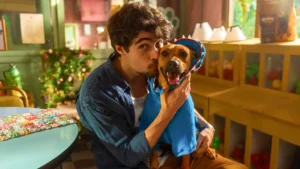 Rafael Vitti abraça o cãozinho vira-lata Amendoim (Caramelo), que usa uma roupa azul, em cena do filme Caramelo da Netflix