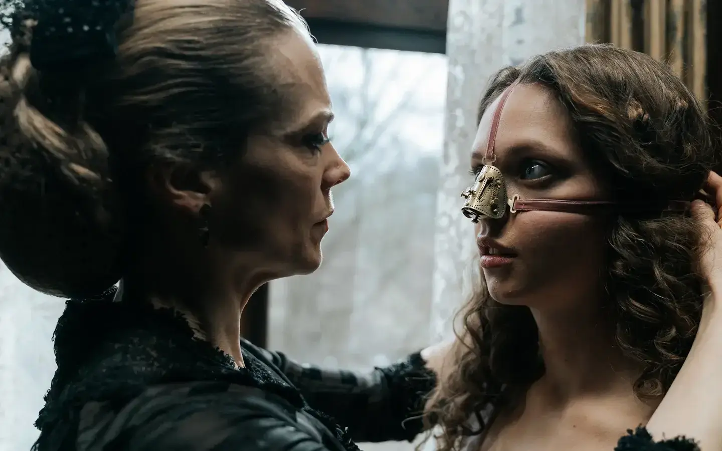 Cena principal de A Meia-Irmã Feia (2025), onde a mãe ajusta uma máscara no rosto da filha, simbolizando o horror dos padrões de beleza