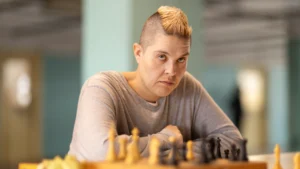 Letícia Rodrigues caracterizada como Sandra Regina Ruiz, a Sandrão, jogando xadrez com uma expressão séria, simbolizando sua posição de líder estratégica na série Tremembé