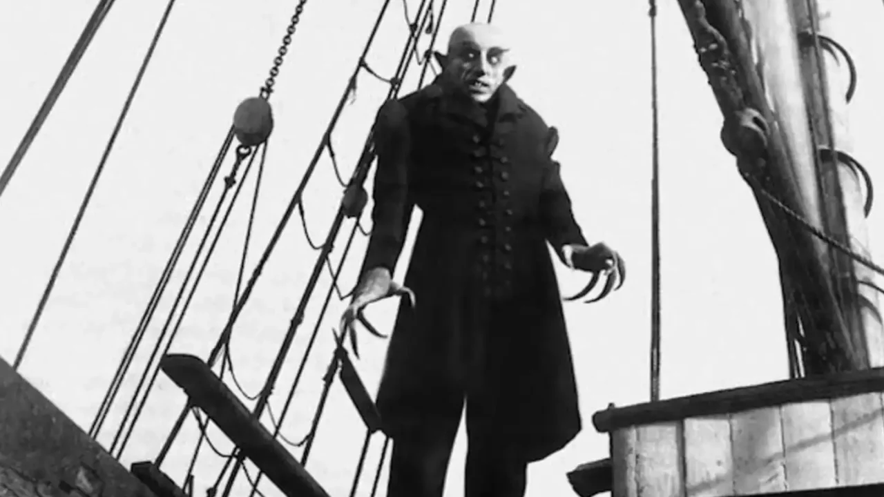 Cena do filme Nosferatu: Uma Sinfonia do Horror (1922) - O personagem principal, Conde Orlok, está parado em uma pose ameaçadora, com um rosto pálido e dedos alongados. (Crédito: TMDB)